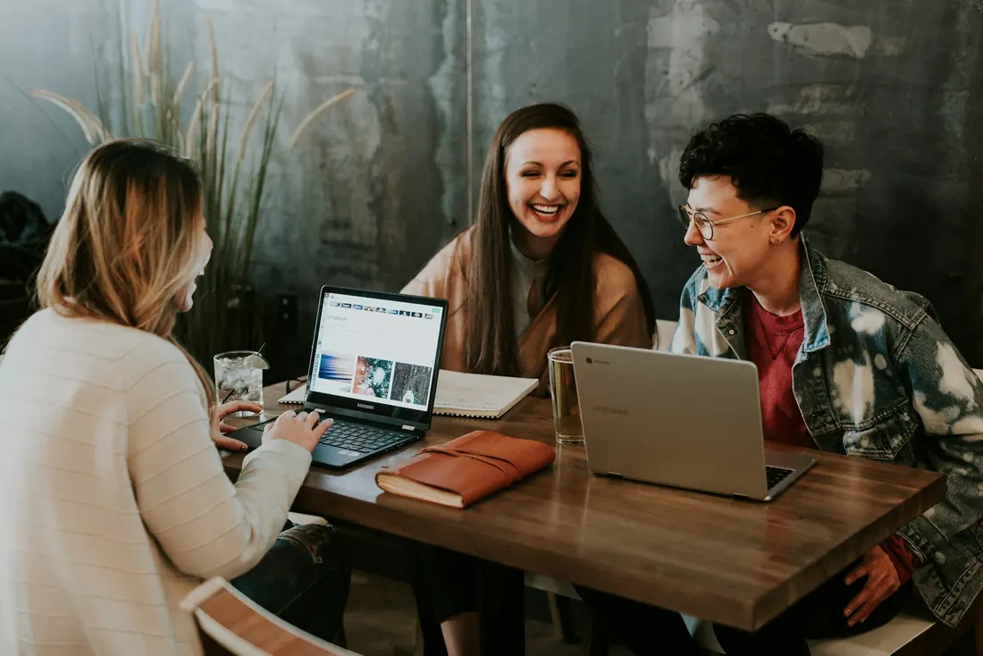 Três estudantes conversando e estudando com notebooks em uma mesa
